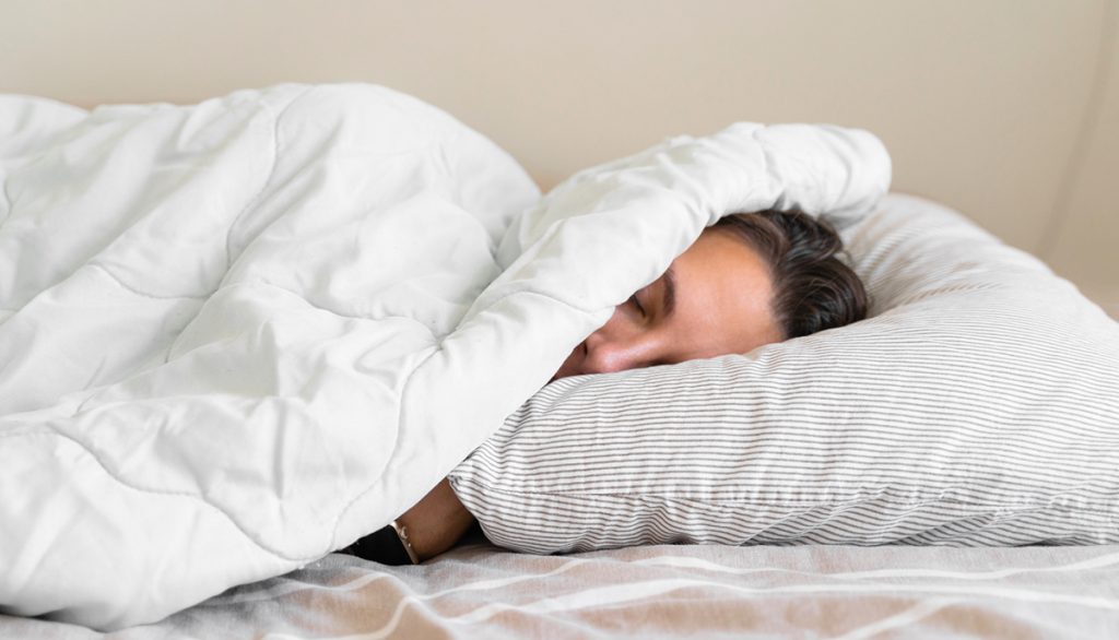Eine Frau die sich wegen Erschöpfung unter einer Bettdecke verkriecht.