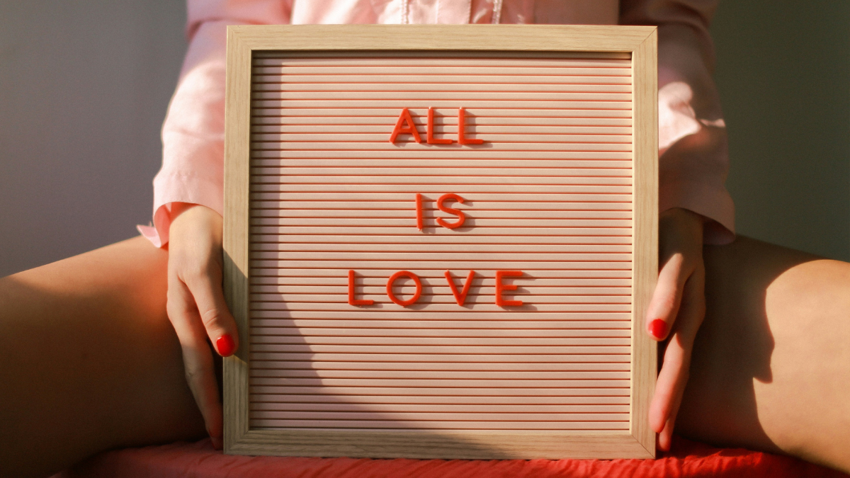 Person hält ein Schild mit der Aufschrift All is Love als Symbolbild für Selbstliebe und Endometriose