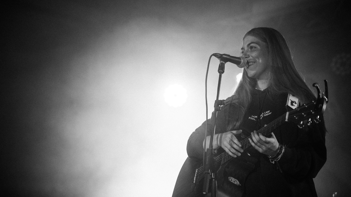 Musikerin Sibuna steht mit Gitarre am Mikrofon auf einer Bühne